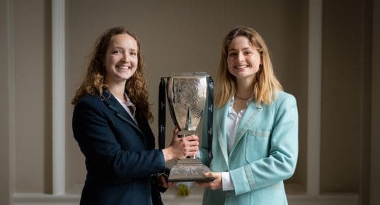 Female Oxford and Cambridge athletes holding the Women's Boat Race trophy