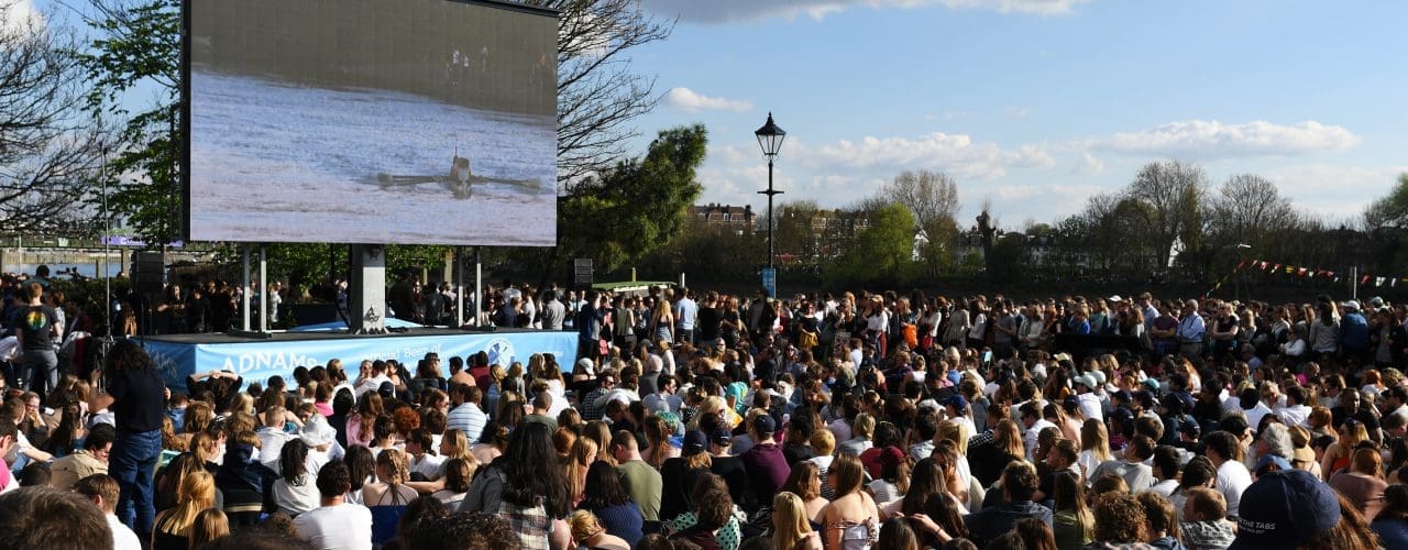 Spectators watching TV coverage of The Boat Race on a big screen outdoors