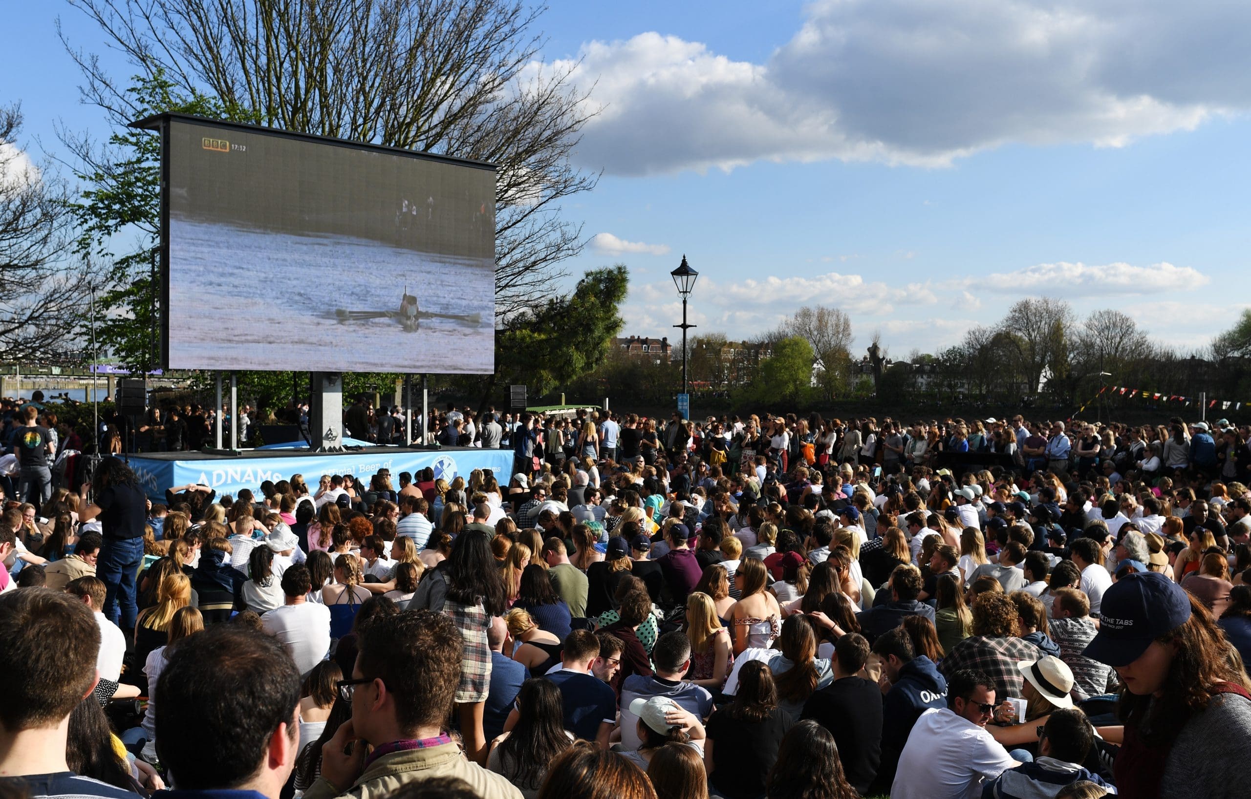Spectators watching TV coverage of The Boat Race on a big screen outdoors
